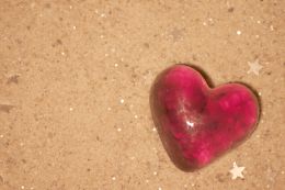 rotes Herz aus Glas mit 2 Glitzersternchen im Sand